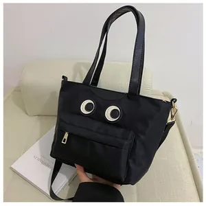 Schwarze Eimer-Handtasche mit Augen-Design auf beigem Sofa im modernen Lifestyle-Look