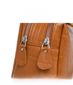 Detail view of the smooth dual zippers and crocodile texture leather on the brown handbag