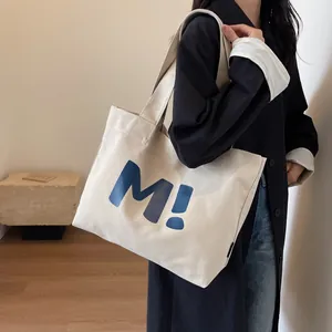 Off-white canvas tote bag featuring a blue 'M!' print with reinforced shoulder straps