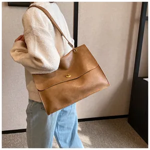 Brown faux leather tote bag with pleated texture and gold lock shown on model indoors