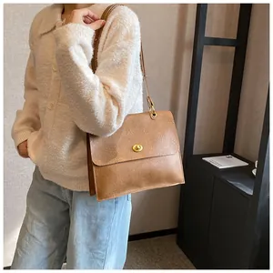 Close-up of vintage beige leather tote bag with gold twist lock on a white cardigan
