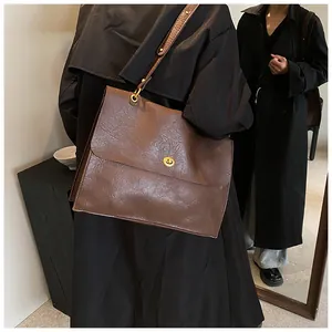 Detail of dark brown vintage leather tote bag with gold metal buckle on black coat