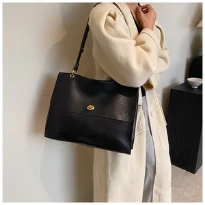 Close-up of black leather tote bag featuring a gold metal twist lock and shoulder strap