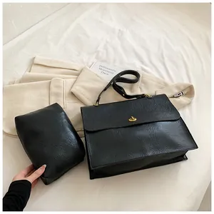 Close-up of black lychee leather tote with gold hardware and matching pouch on soft linens