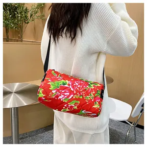Detail of red floral quilted cylinder bag with black strap worn by a model in a white sweater