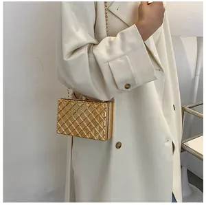 Elegante goldene Abendtasche mit Rautenmuster und Kettenriemen auf einem Trenchcoat