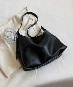 Close-up of black litchi grain leather tote bag with wide strap on white blazer