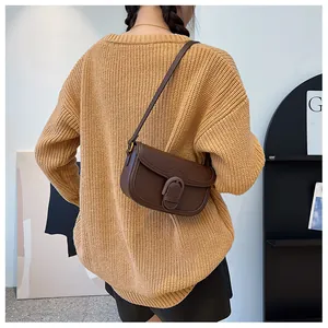 Gros plan d'un sac besace marron foncé avec boucle tressée sur un pull en maille camel