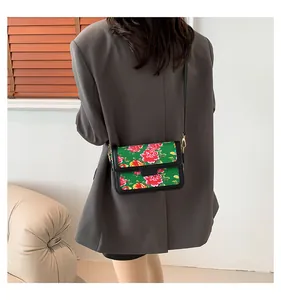 Detail of green floral crossbody bag with peony pattern and metallic gold buckle on model