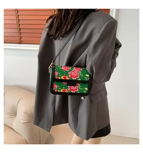Detail of green crossbody bag with red peony floral pattern and black trim finish