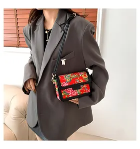 Crossbody bag with red floral peony patterns and black trim shown on a model