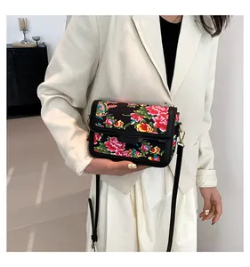 Close-up of ethnic floral and phoenix pattern on a black crossbody bag worn with a beige blazer