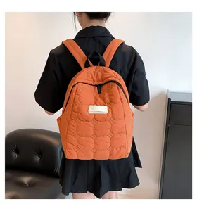 Rear view of orange quilted backpack with padded straps on model in minimalist room