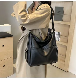 Detailed close-up of large black leather hobo bag worn with a beige trench coat