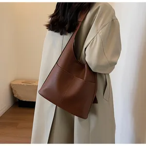 Close-up of brown pebbled leather tote bag with wide strap on a model wearing a beige trench coat