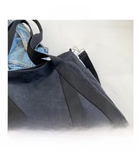 Close-up of black canvas tote bag with metal hooks, woven straps and denim backdrop