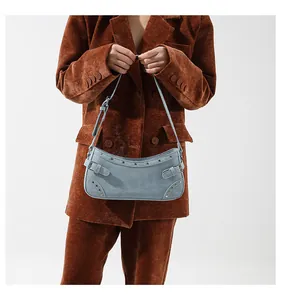 Détail du sac d'épaule en denim bleu clair avec clous porté sur un blazer en velours