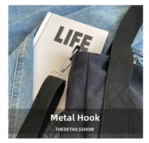 Detail of silver metal hook and wide fabric strap on black canvas tote bag