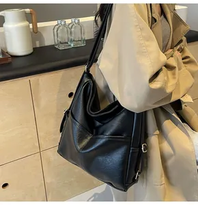 Detail of a large black leather bucket bag styled with a beige trench coat for a chic look