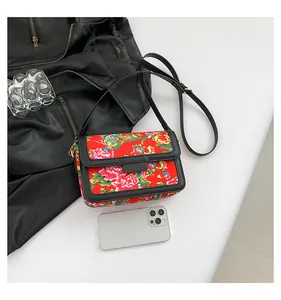 Top view of traditional red floral crossbody bag with black strap on a desk with props