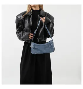 Sac baguette en denim bleu avec rivets argentés porté par un mannequin en veste de cuir