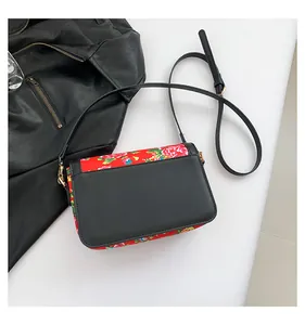 Detail of floral embroidery on black leather crossbody bag with gold hardware