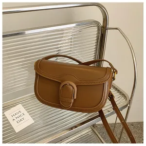 Détail d'un sac besace en cuir mat marron avec rabat et large boucle sur une chaise