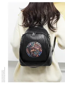 Detail of black PU leather backpack with gold elephant patch on model wearing white sweater