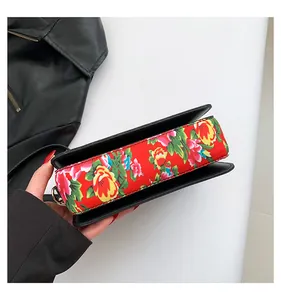 Detail of crossbody bag featuring red floral fabric on black leather side and metal loop