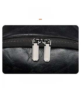 Close-up of dual metal zippers on black lychee-grain leather backpack with polished hardware