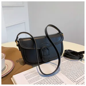 Détail d'un sac besace en cuir noir avec ferrures dorées sur un bureau blanc épuré