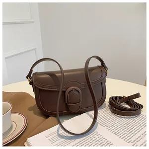 Détail d'un sac besace rétro en cuir marron avec bandoulière sur table blanche
