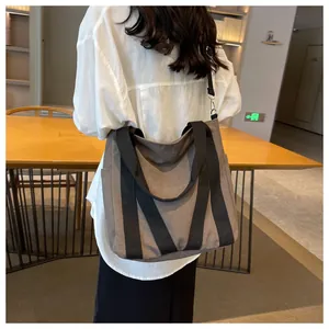 Detail of a large brown canvas tote bag featuring durable black handles and a side pocket