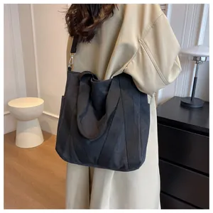 Detail of a large black canvas tote bag with adjustable shoulder strap on a model