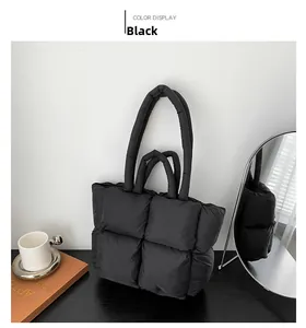 Macro detail of black quilted puffer tote bag with dual straps on a wooden table