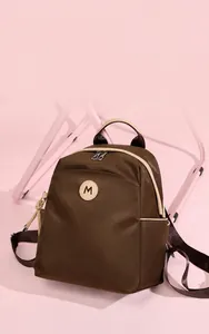 Detail of coffee brown oxford backpack with white piping and metallic M logo accent