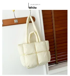 Detail of white quilted down tote bag hanging on wooden hook against white wall