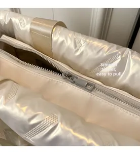 Close-up of smooth silver metal zipper on white puffer bag with quilted nylon texture