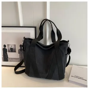 Detail of minimalist black canvas tote bag showing side pockets and shoulder strap attachment