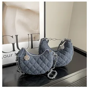 Detalle de bolsos media luna de mezclilla con acolchado, cadenas de plata y dijes de camelia