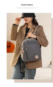 Detalle de mochila gris de tela oxford con cremallera metálica y emblema M naranja