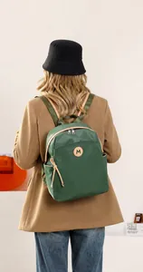 Detailed back view of a green oxford backpack with brown leather trim on a model