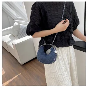 Detalle de bolso medialuna de mezclilla azul oscuro con cadena y colgante de flor
