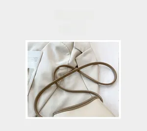 Détail du sac seau beige en cuir grainé avec bandoulière marron sur veste blanche
