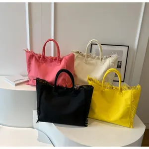 Détail de cabas en toile colorés avec bords effilochés en rose, crème, noir et jaune