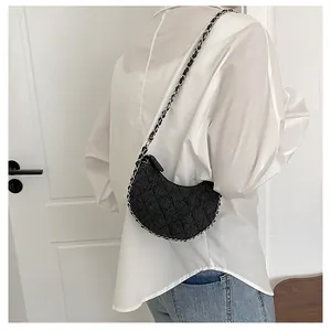 Detalle del bolso bandolera de media luna negro con textura acolchada y correa de cadena