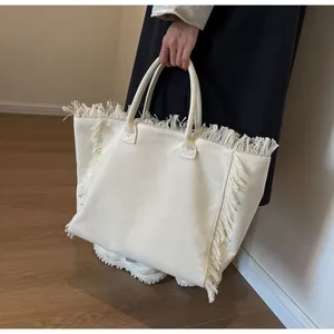 Gros plan d'un cabas en toile crème avec des détails de franges et une double poignée