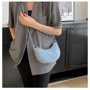 Detalle del bolso de media luna en denim azul claro con acolchado de rombos y cadena plata