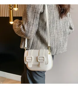 Detail view of a cream leather saddle bag with double buckles worn over the shoulder