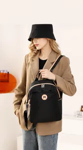 Close-up of black nylon backpack featuring a round M logo and light-colored pocket trim